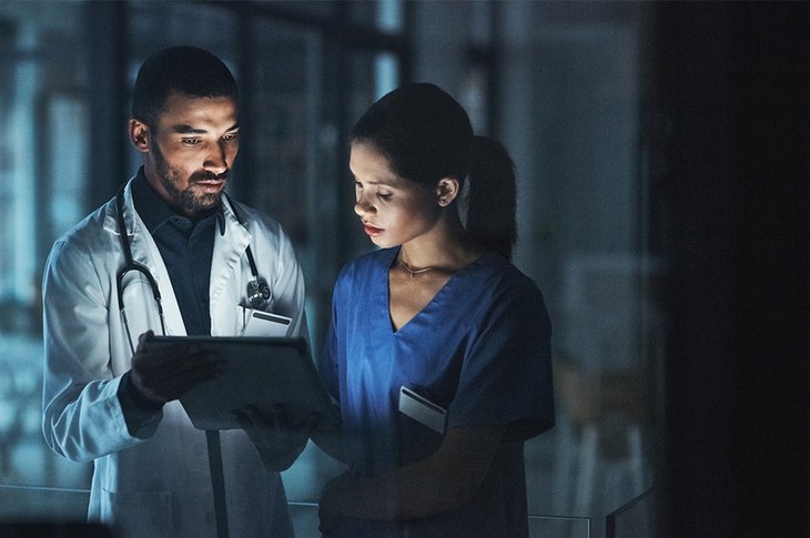 Ein Arzt in weißem Kittel und eine Ärztin in blauem Hemd sehen sich eine Akte an