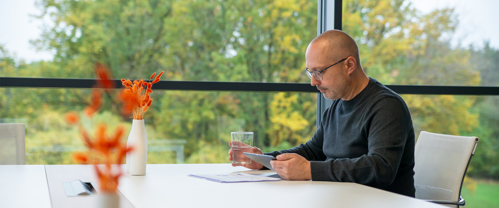Holger Fuchs sitzt mit einem Ipad und einem Glas Wasser an einem Tisch vor einigen Dokumenten