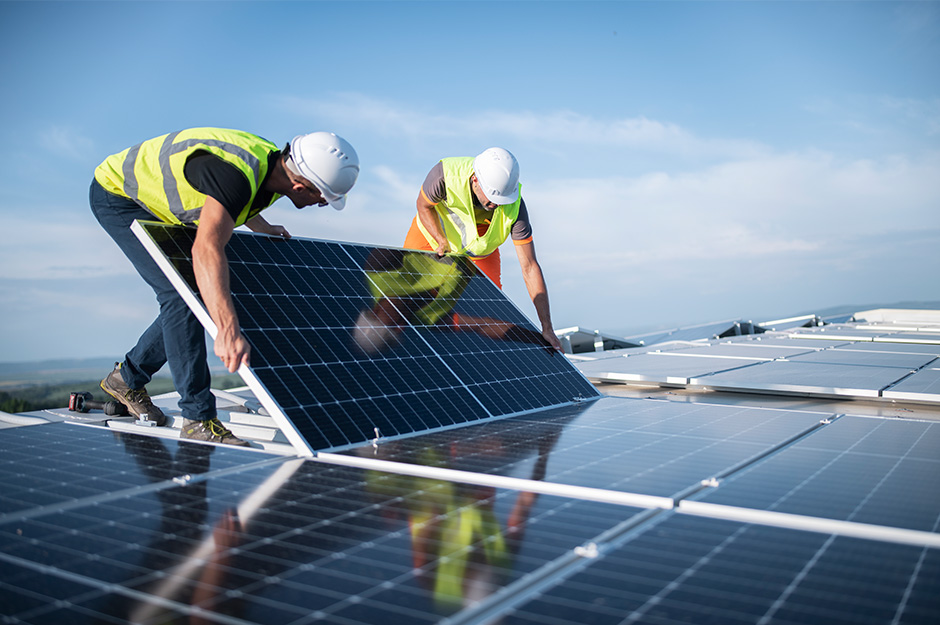 Zwei Arbeiter bringen ein Solarpanel auf einem Dach mit vielen Panelen an